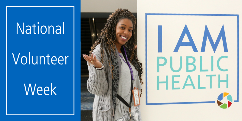National Volunteer Week. Woman posing next to a sign that says "I am public health"