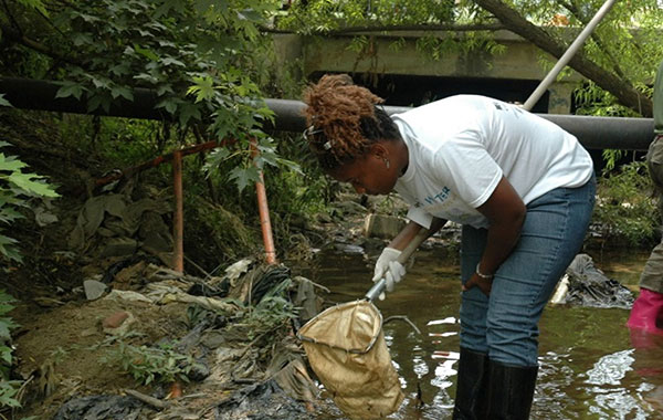 woman in rubber boots scooping water waste into net