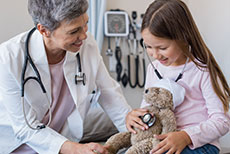 woman doctor helping girl check teddy bear with stethoscope