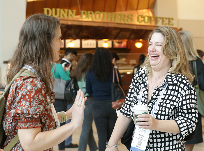 Two people stand in a conference room lobby laughing and talking. 