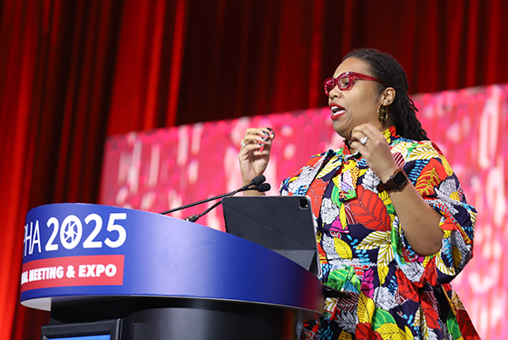 New APHA President Nandi Marshall wears a colorful dress and speaks from behind a lectern on a large stage.