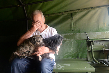 A distressed man has his hand over his face as two dogs sit on his lap
