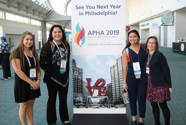 four smiling women in front of APHA 2019 sign