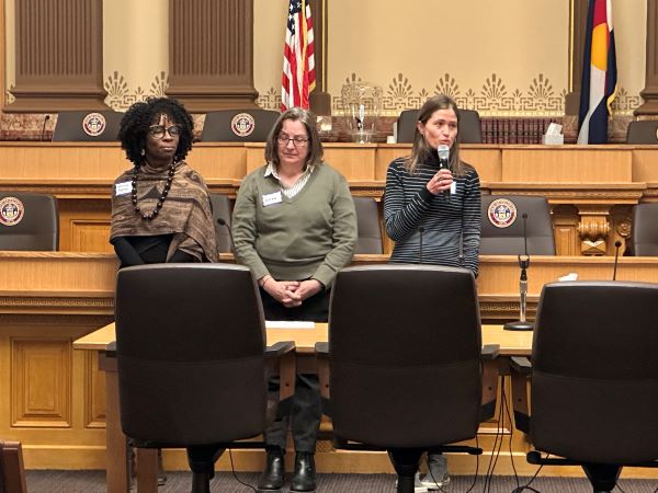 Three members of the Colorado Public Health Association in a government building, one speaking into a microphone