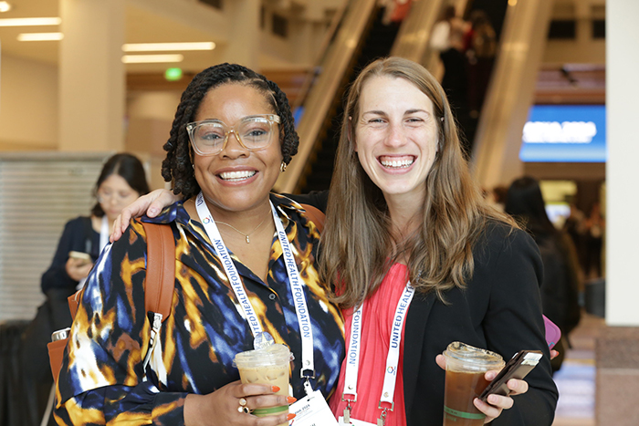 Two people hold coffee cups and stand together and smile for the camera. 