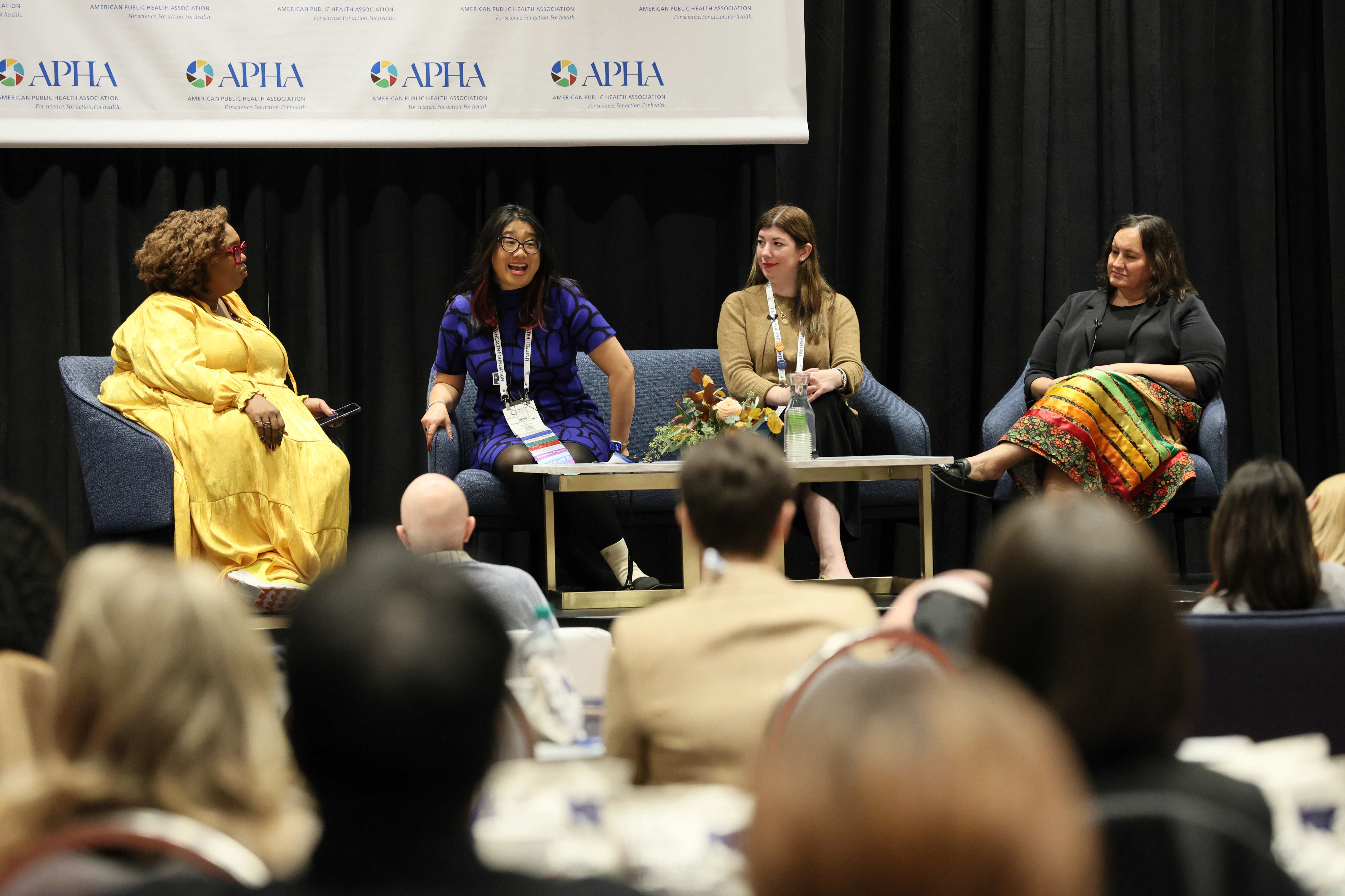 Diverse group of women sitting on stage with people in the audience