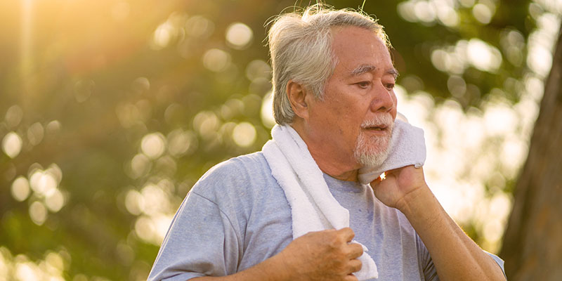 A man working out and wiping his face with a towel, outside with sun shining
