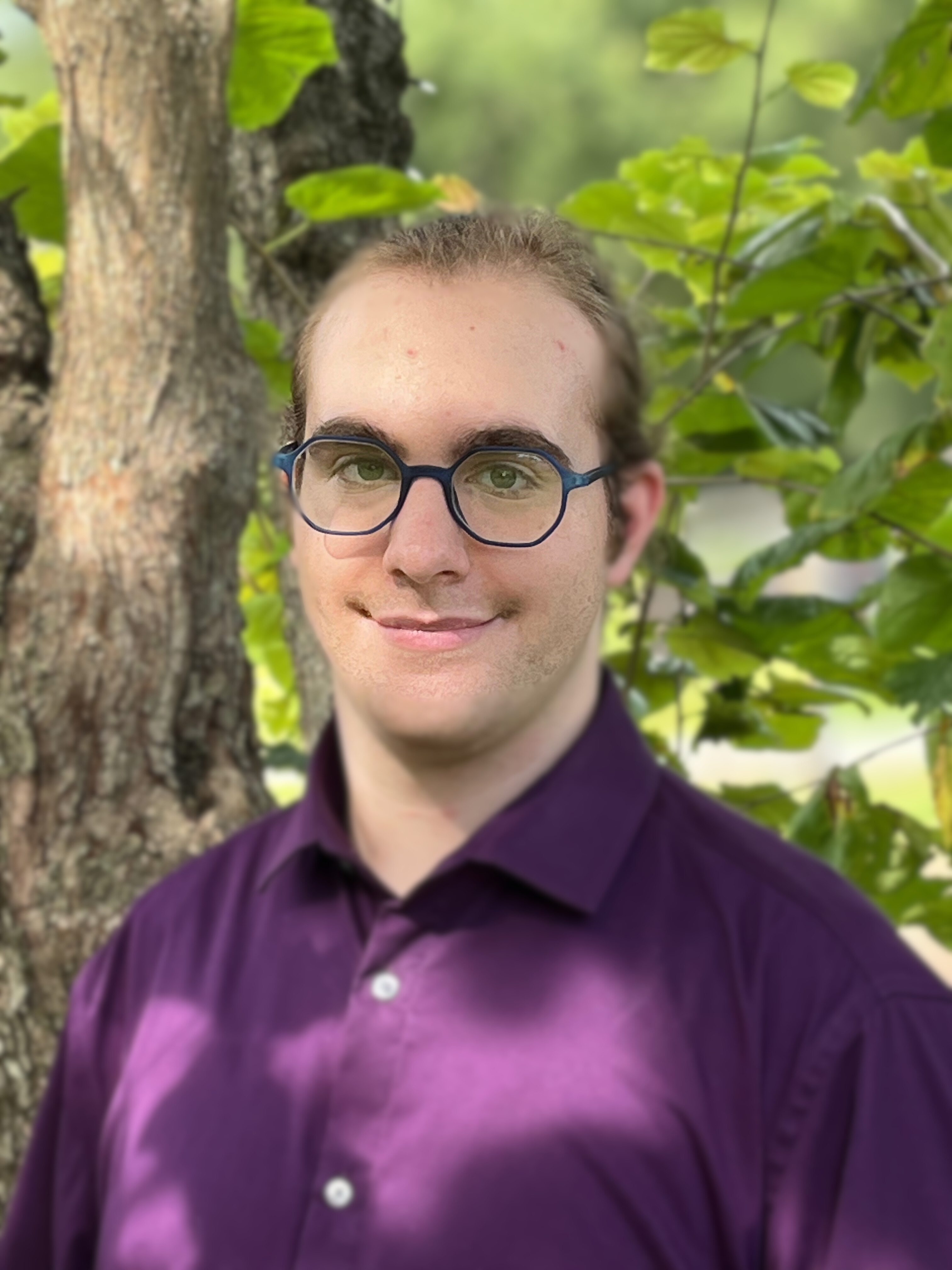 White person smiling at the camera wearing glasses and a purple collared shirt, standing outside