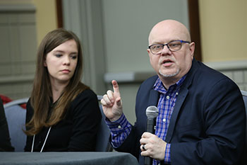 woman listens as man with microphone speaks