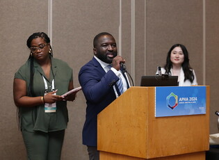 Woman speaking at a podium at APHA annual meeting with two other people near him