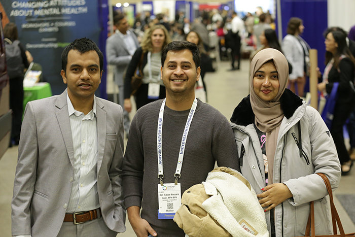 Two men and a woman stand next to each other in the Expo Hall and facing the camera. 