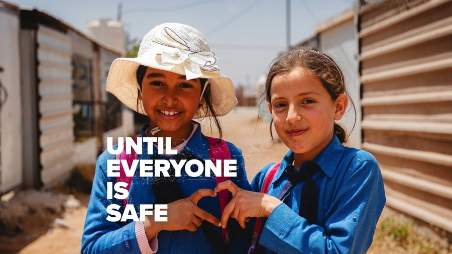 Two little kids in front of shelters wearing blue shirts making a heart with their hands