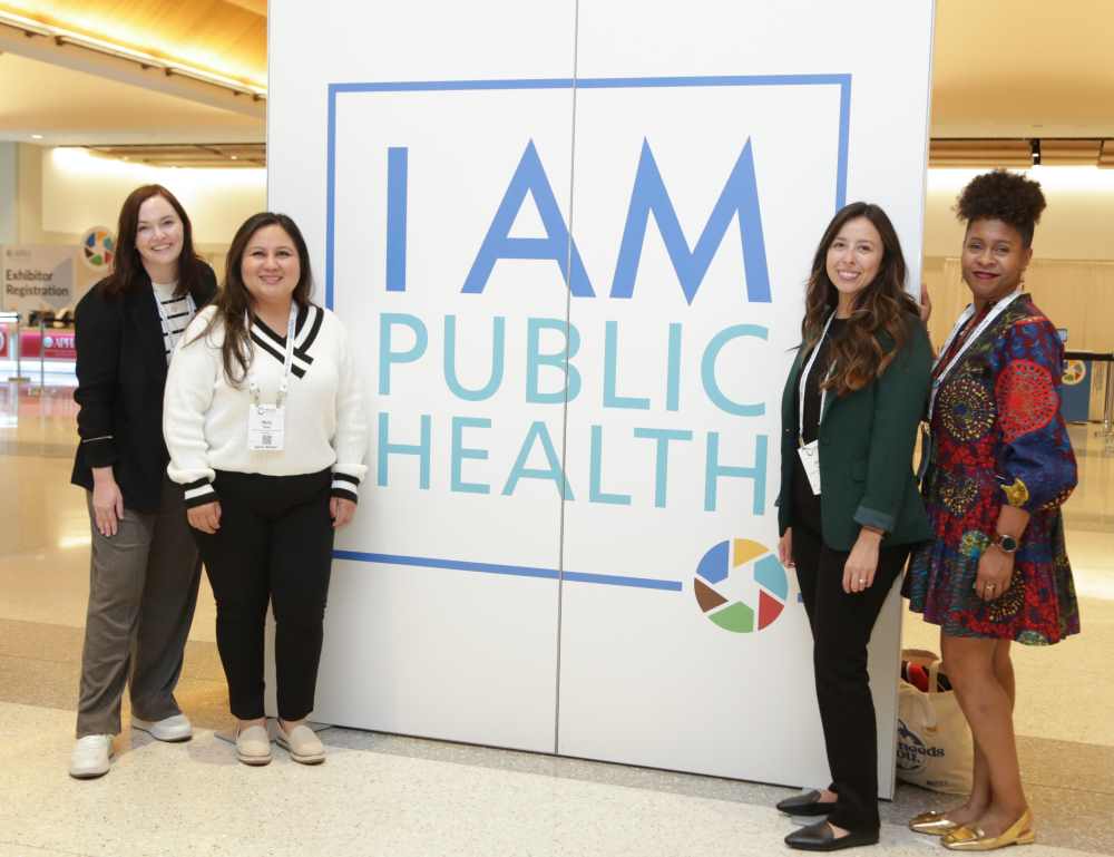 Photo of 4 women next to a sign that reads I AM PUBLIC HEALTH