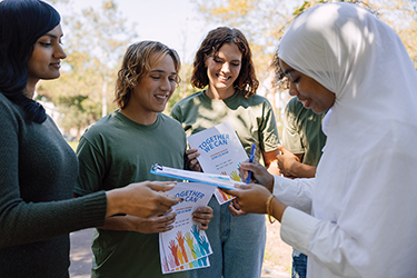 People of various ethnicities share handouts with one another about an event