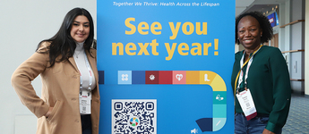 Two women pose on either side of a free-standing APHA banner that says "See you next year!"