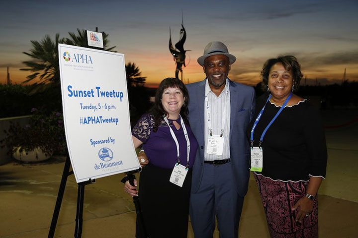 two women and one man smiling in front of Sunset Tweetup sign