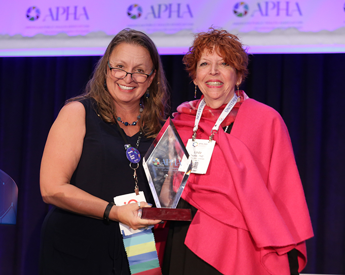 Two women pose and smile for the camera as one holds an award. 