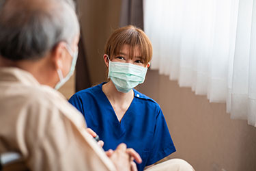 masked health care worker talking to masked older man