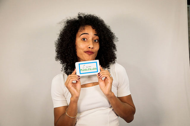 smirking woman displaying I am public health tag