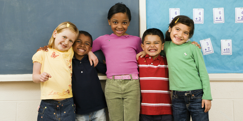 five smiling kids arm in arm in front of a chalkboard