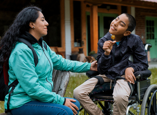 Happy disabled child smelling a flower with his mother outdoors 