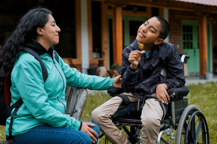 Happy disabled child smelling a flower with his mother outdoors 