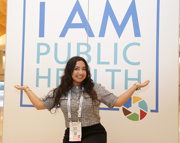 A person poses in front of a sign that says I Am Public Health. 