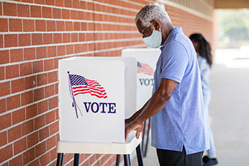 mask-wearing man at outdoor voting booth