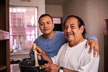 Two men smile for the camera as they prepare a meal