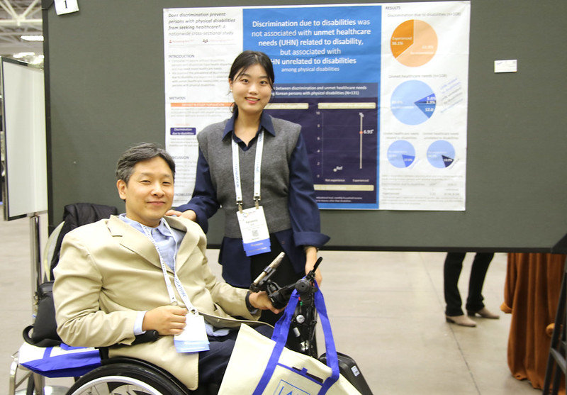 Two presenters giving a poster presentation at the APHA annual meeting, one in a wheelchair