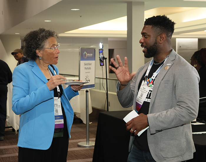 A woman holds a plate while listening to a man talk to her at the APHA President's Reception. 
