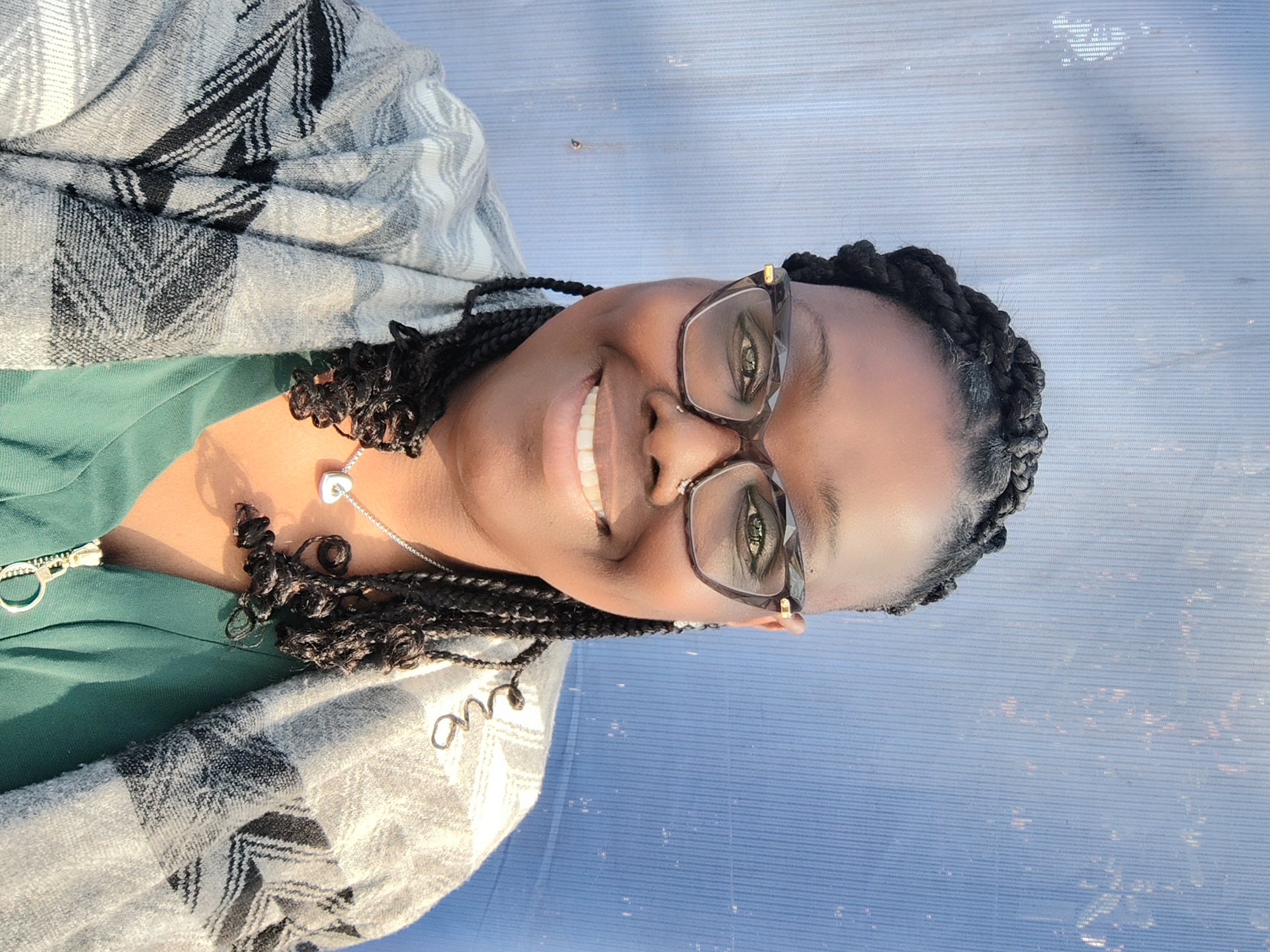 A Black woman with braids in front of a blue background, smiling with glasses on. 