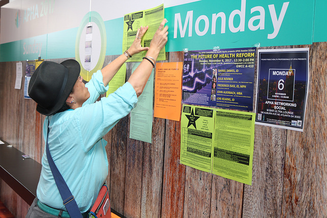 person in hat placing sign on bulletin board