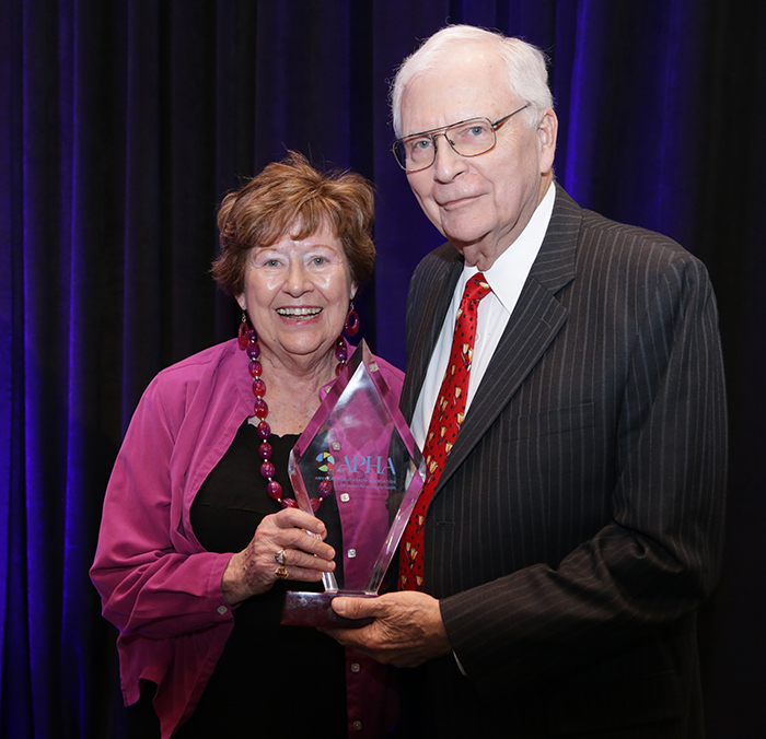 A woman and man pose for the camera while holding an award. 