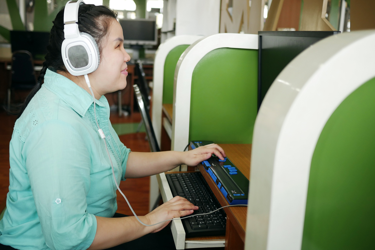 Asian woman with blindness disability using computer with refreshable braille display or braille terminal a technology assistive device for persons with visual impairment in workplace.