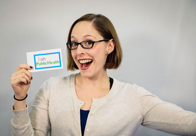 smiling woman displaying I am public health tag