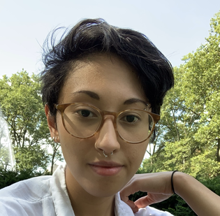 A person with glasses in a white shirt with short black hair outside with trees in the background 