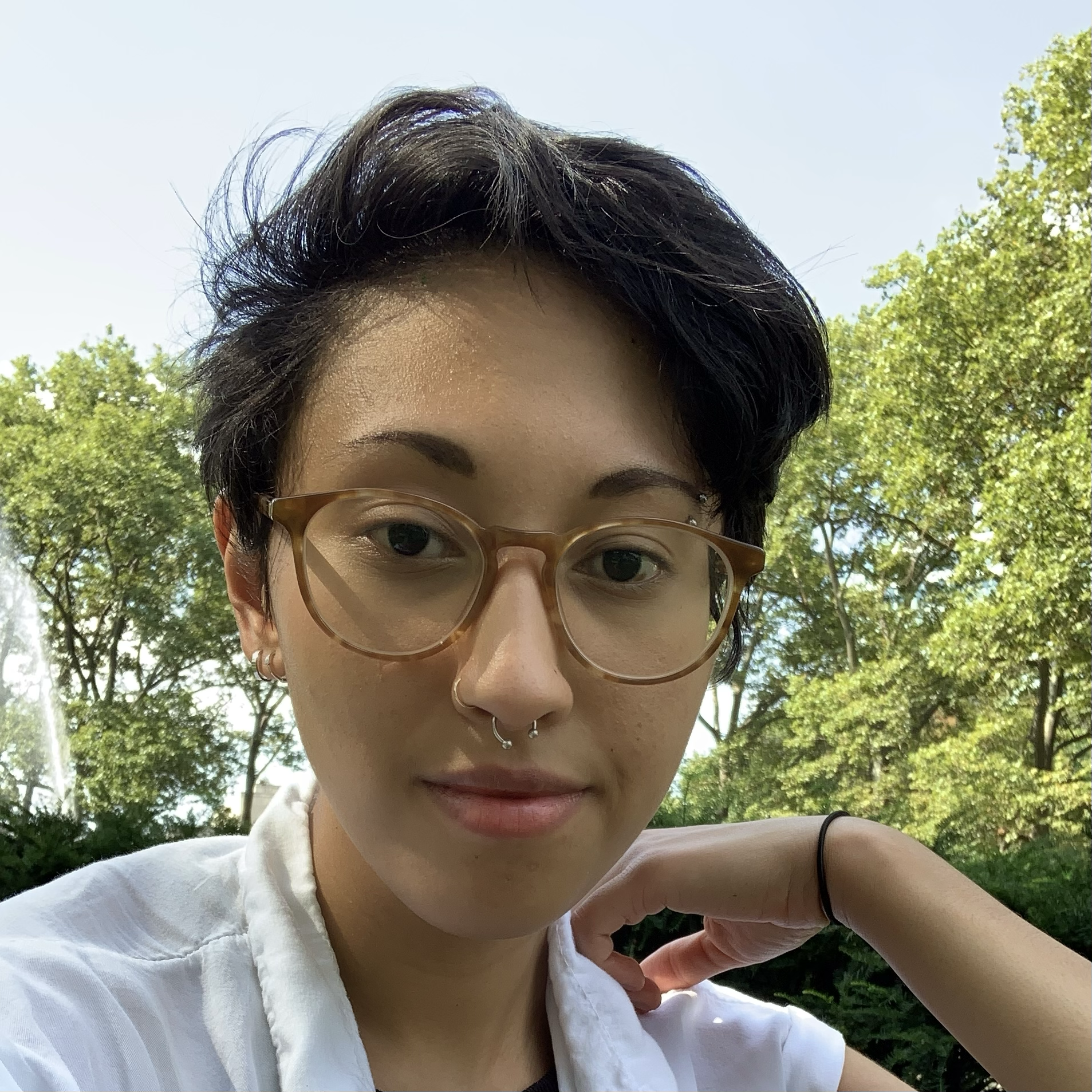 A person with glasses in a white shirt with short black hair outside with trees in the background 