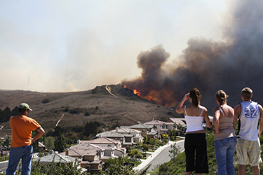 Spectators watch as a recent southern california brush fire burning extremely close to homes.