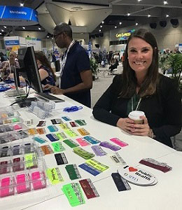 smiling Caitlin Sarlo at membership booth with colorful badge ribbons on display